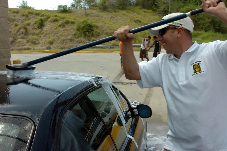 Volunteer scrubbing a car roof with a long-handled brush