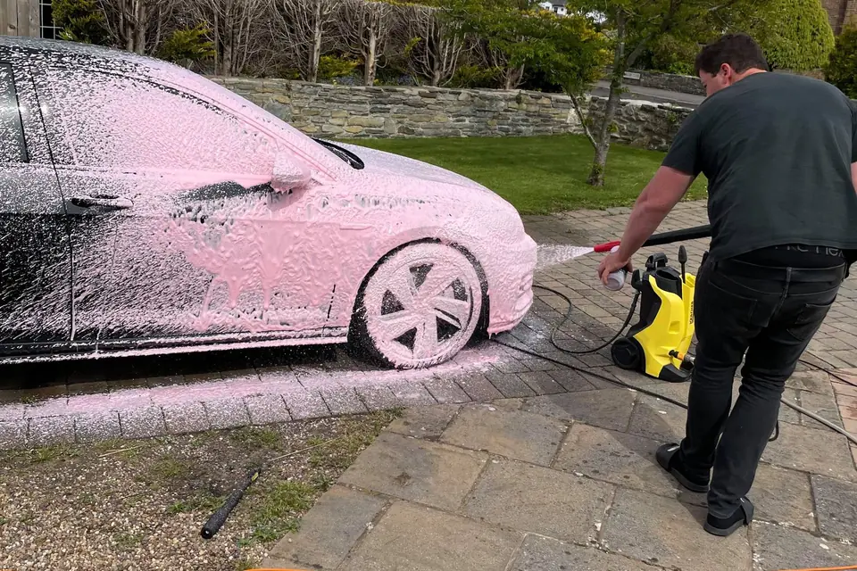 Car covered in pink foam being rinsed on a driveway