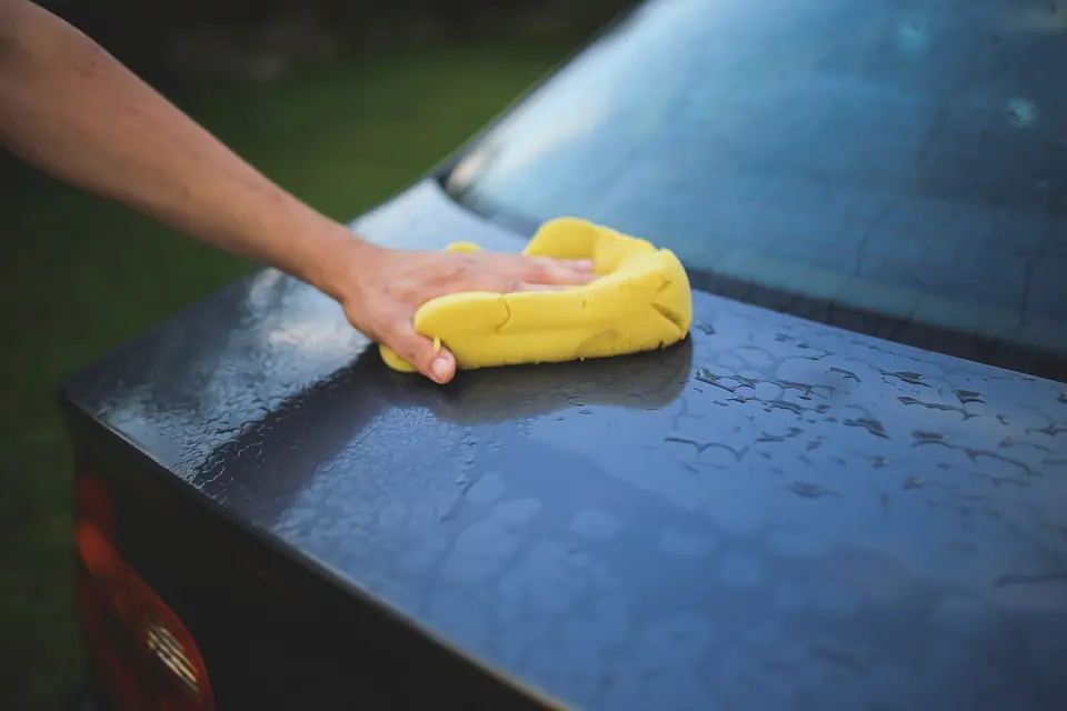 Hand washing a dark car with a soapy yellow sponge